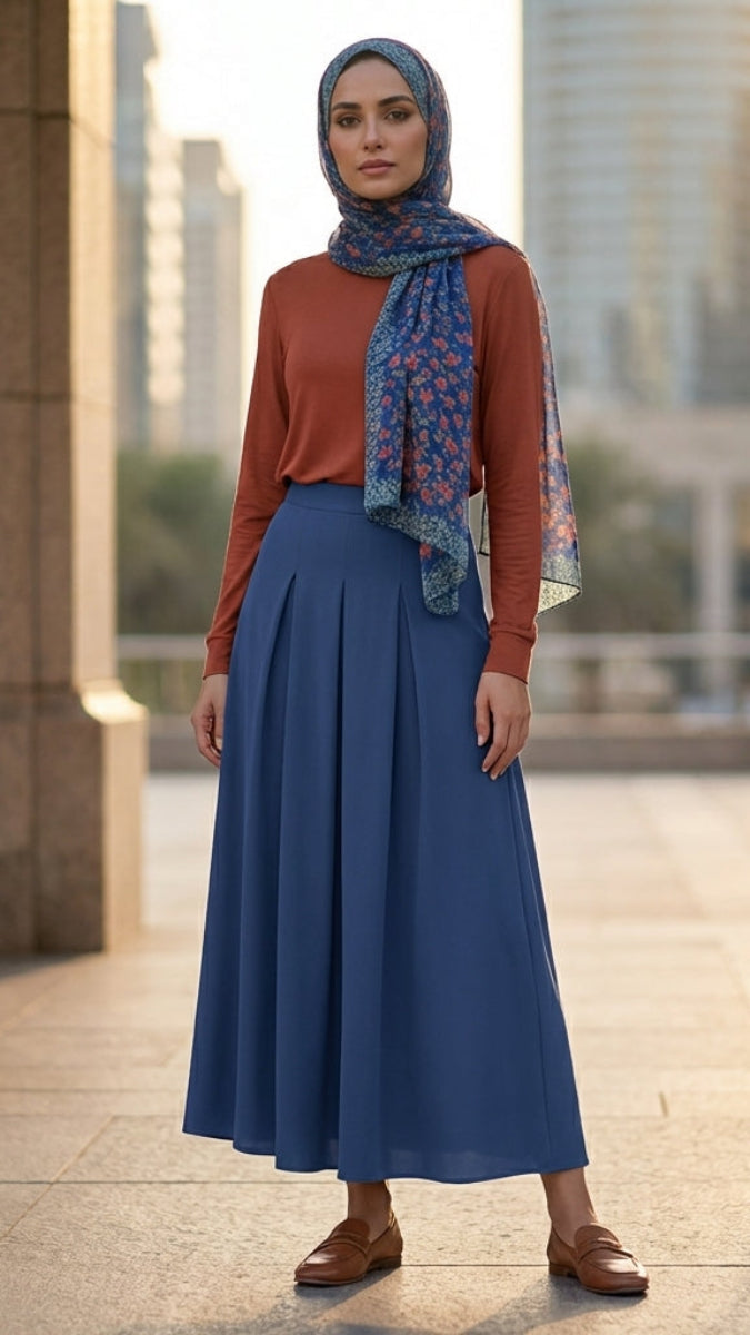 Woman wearing a blue hijab, brown top, and blue skirt standing in an urban setting.