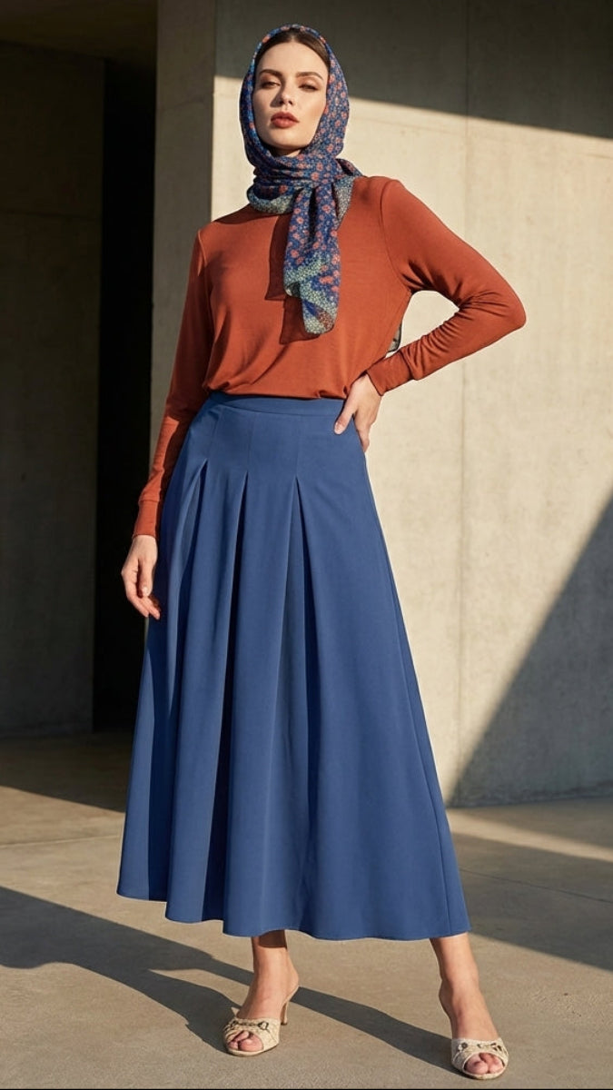 Woman wearing a rust-colored top and blue skirt with a patterned headscarf in an urban setting.