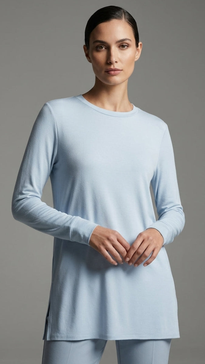 Woman wearing a light blue long-sleeve top and pants against a gray background