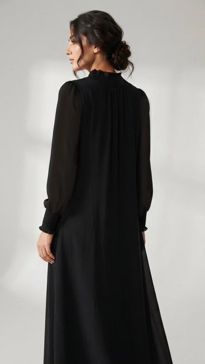 A woman wearing a long black dress, photographed from the back against a plain light gray studio background.