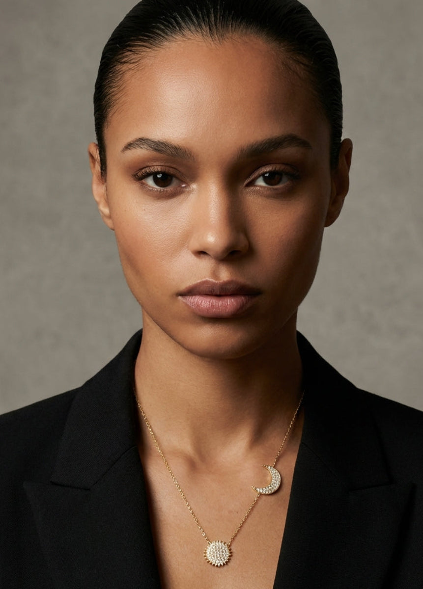 Woman wearing a black blazer and gold necklace against a neutral background