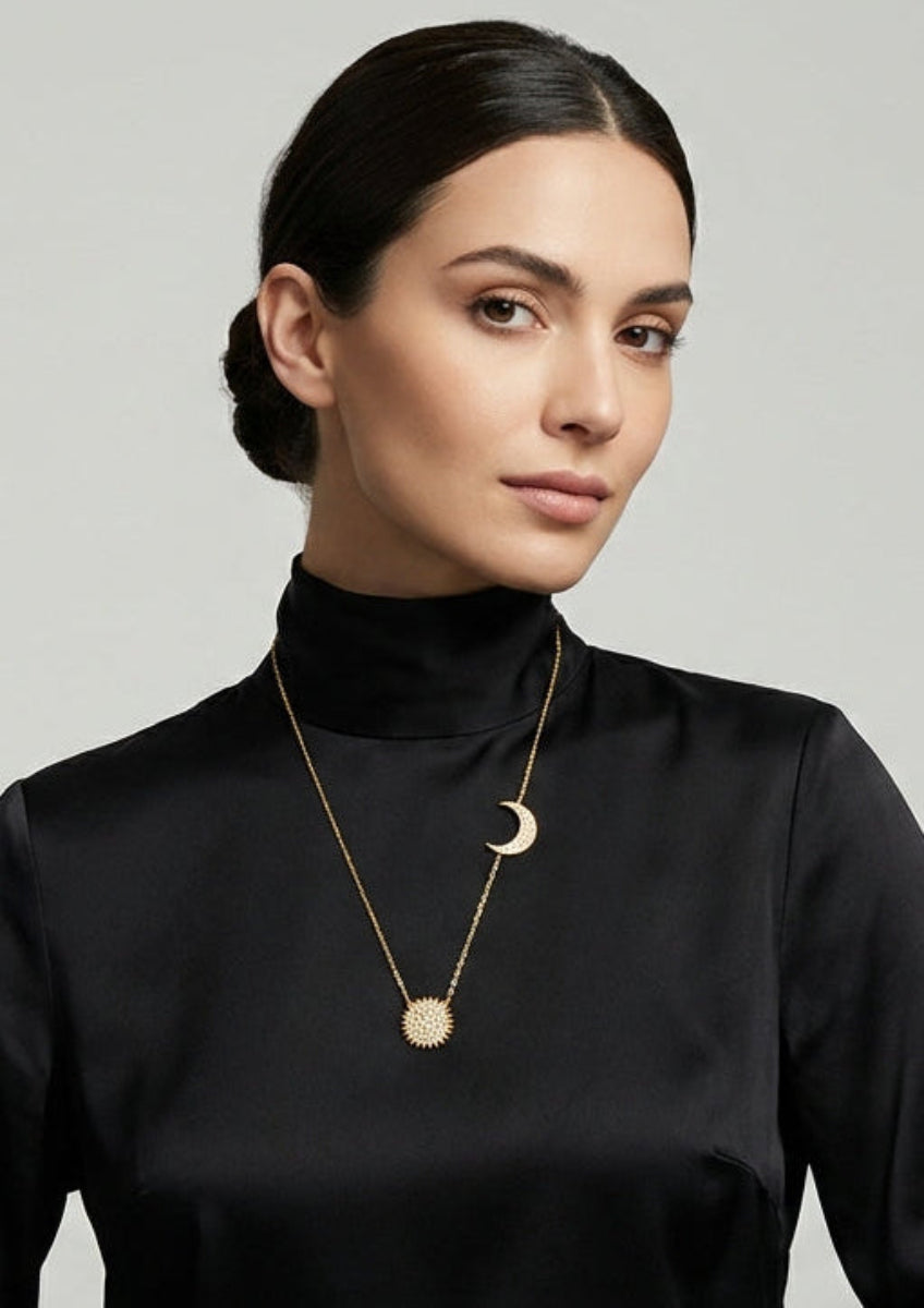 Woman wearing a black turtleneck and gold necklace against a gray background