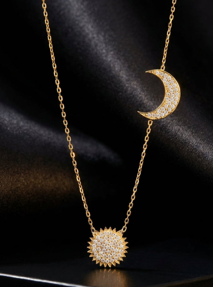 Gold necklace with moon and sun pendants on a black background