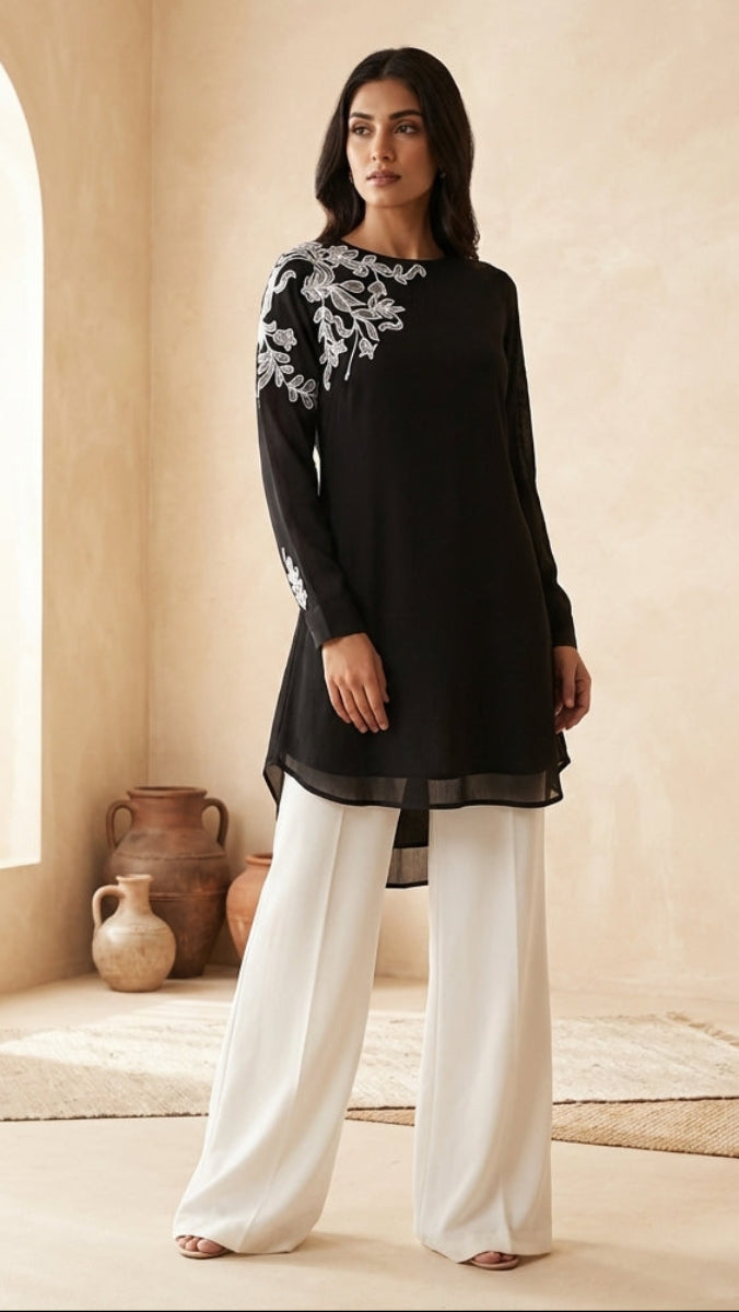 Woman wearing a black outfit with white embroidery in a softly lit room.