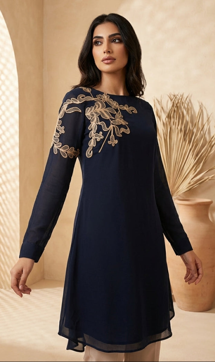 Woman wearing a navy blue dress with gold embroidery in a warm-toned room.