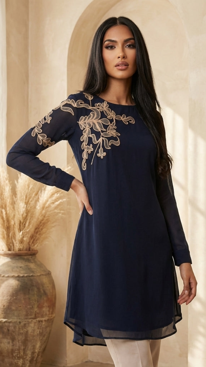 Woman wearing a navy blue dress with gold embroidery in a warm-toned interior setting.