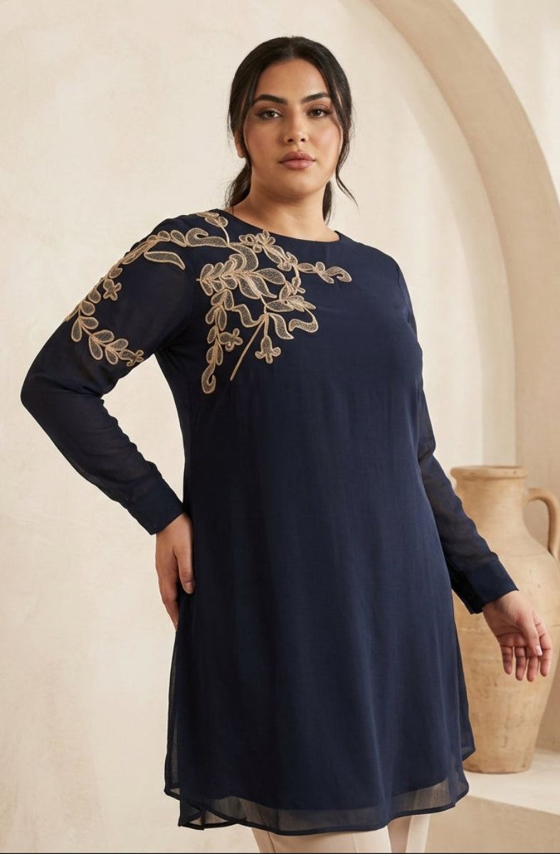 Woman wearing a navy blue dress with gold embroidery in an indoor setting.