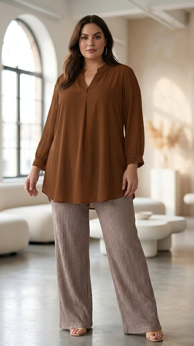 Woman wearing a brown blouse and beige pants in a modern living room.