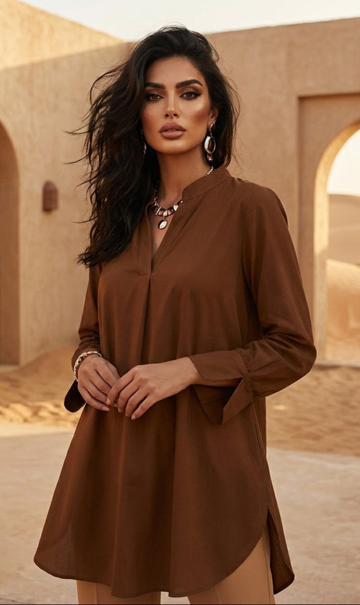 Woman in a brown dress standing in a desert setting with sand and arches in the background.