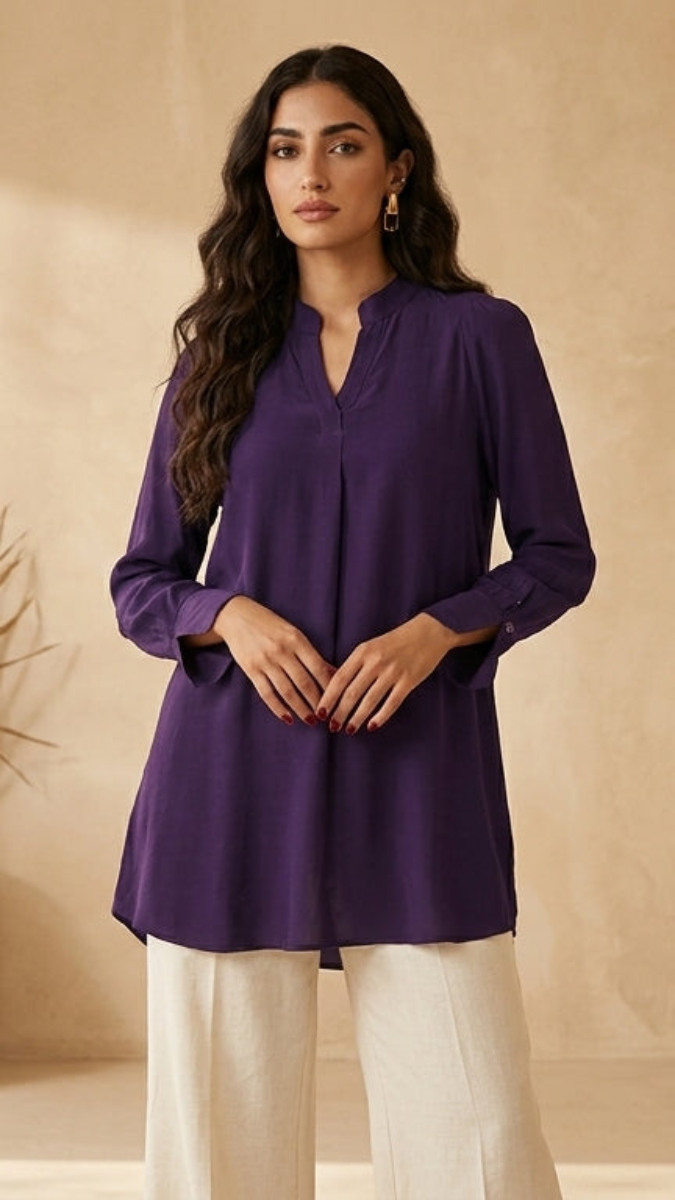 Woman wearing a purple kurta with white pants in a warm-toned room.