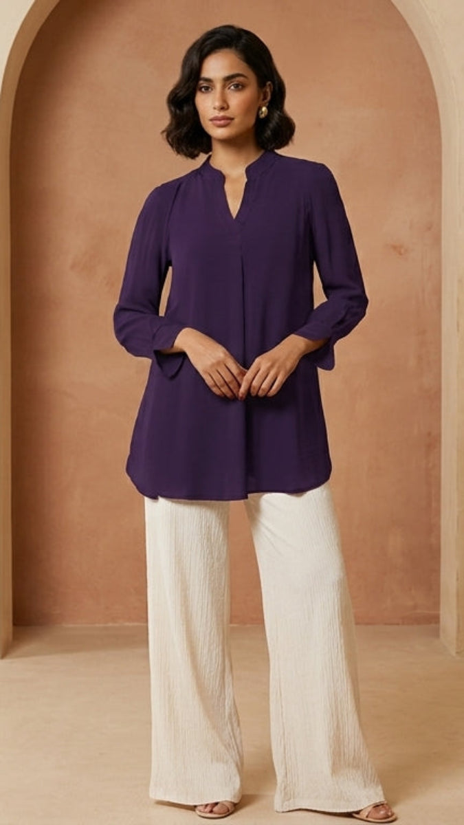 Woman wearing a purple top and white pants standing in a beige room with an archway.