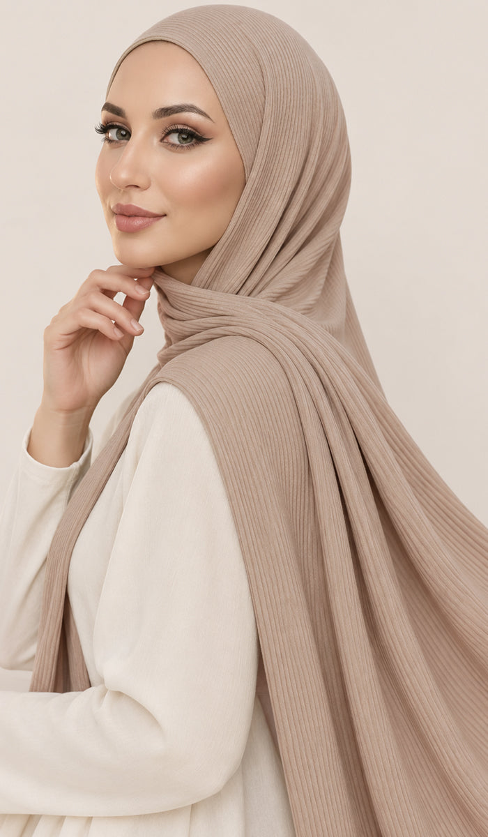 A woman wearing a beige ribbed hijab and a cream-colored long-sleeve top, posing against a solid light beige background.
