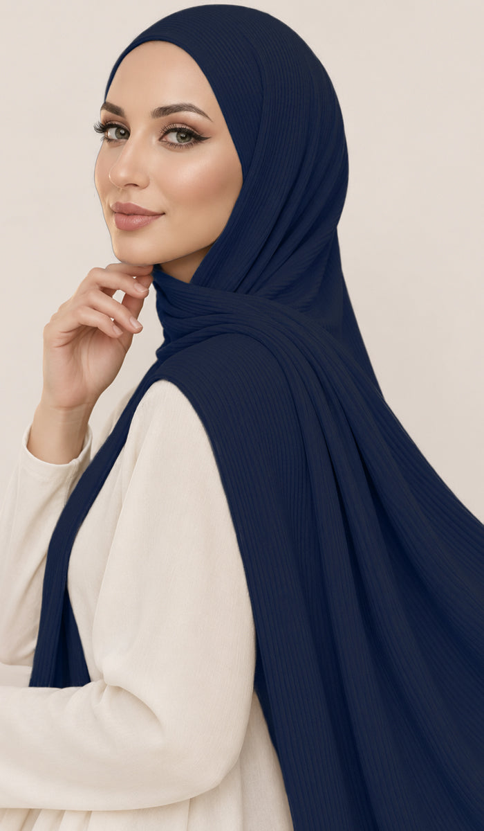 A woman wearing a dark navy blue ribbed hijab and a cream-colored long-sleeve top, posing against a solid light beige background.