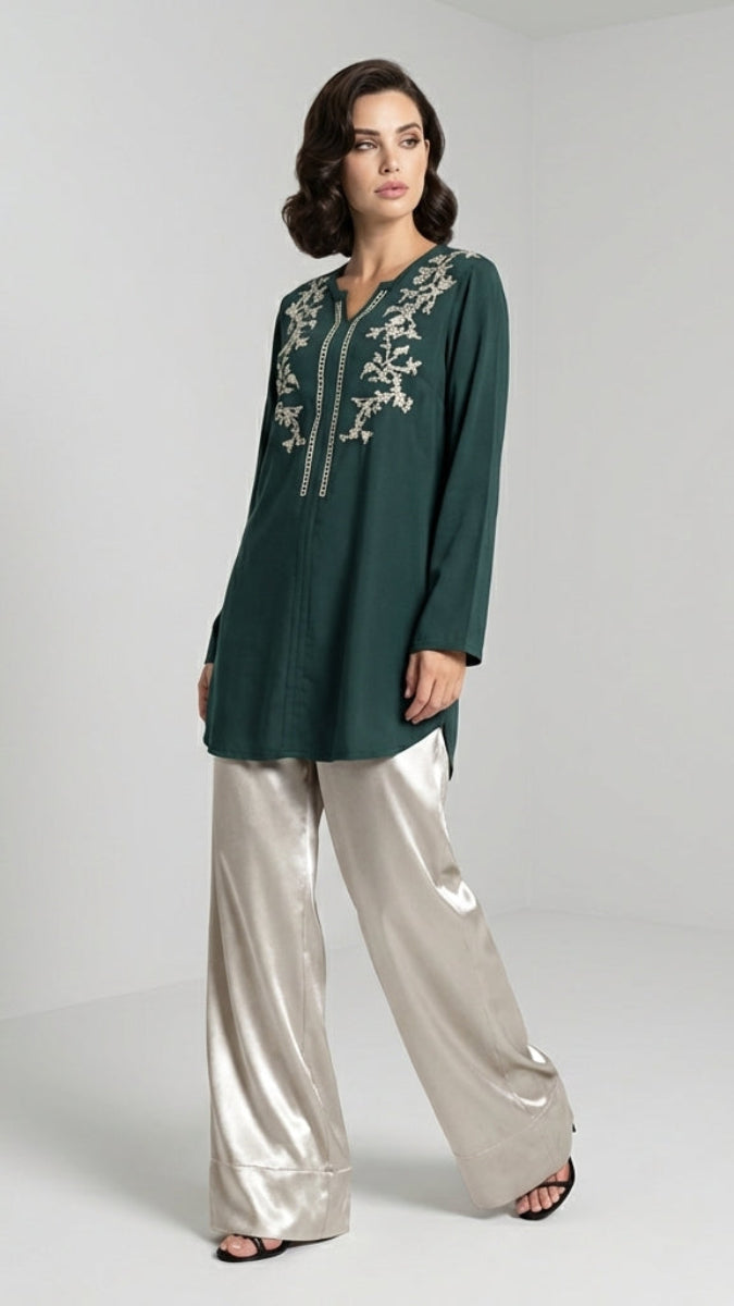 Woman wearing a green embroidered top and silver pants on a white background