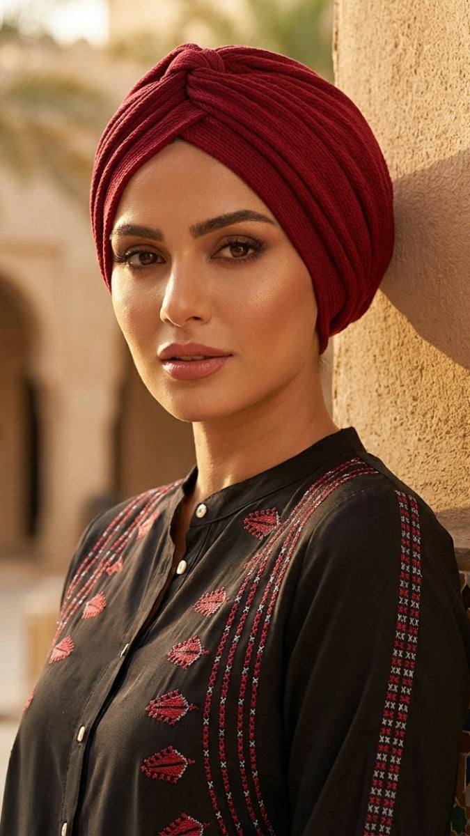 Woman wearing a red turban and black embroidered outfit in an outdoor setting.