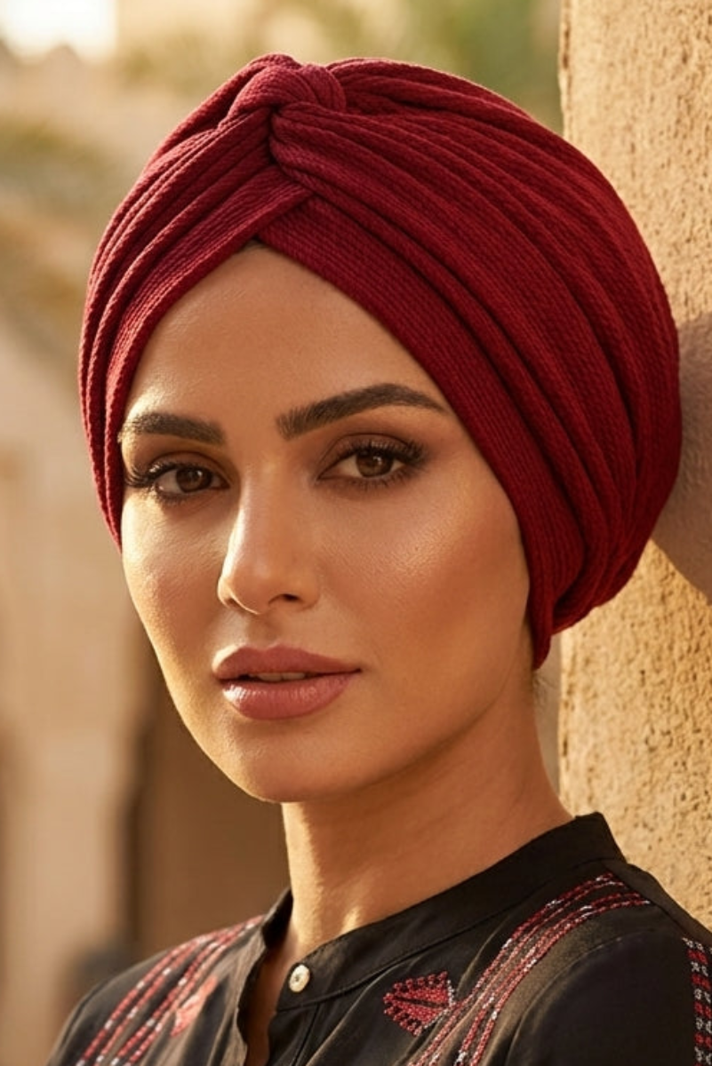 Woman wearing a red turban and black embroidered outfit in an outdoor setting.