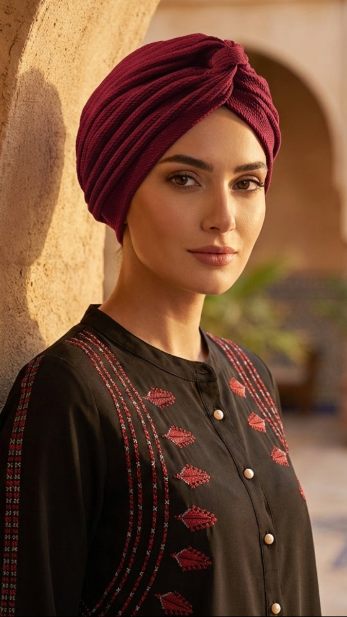 Woman wearing a red turban and black embroidered outfit in a decorative outdoor setting.