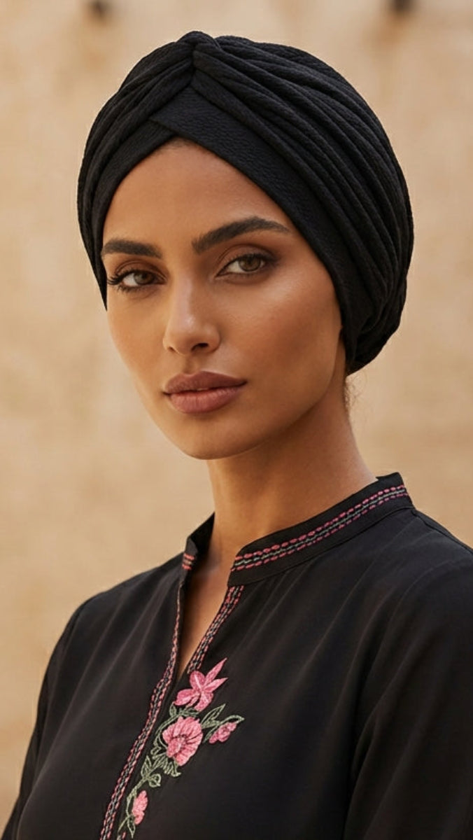 Woman wearing a black embroidered dress and headscarf in an outdoor setting