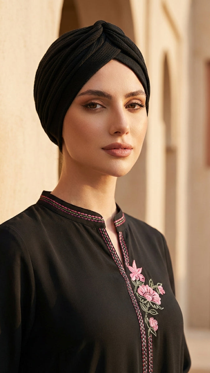 Woman wearing a black embroidered dress and headscarf in an architectural setting