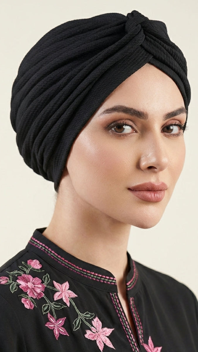 Woman wearing a black abaya with pink floral embroidery and a matching black turban.