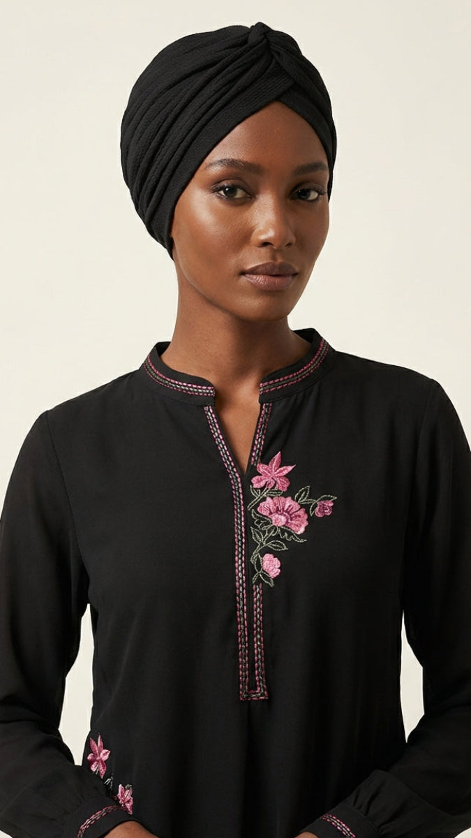 Woman wearing a black top with floral embroidery on a beige background