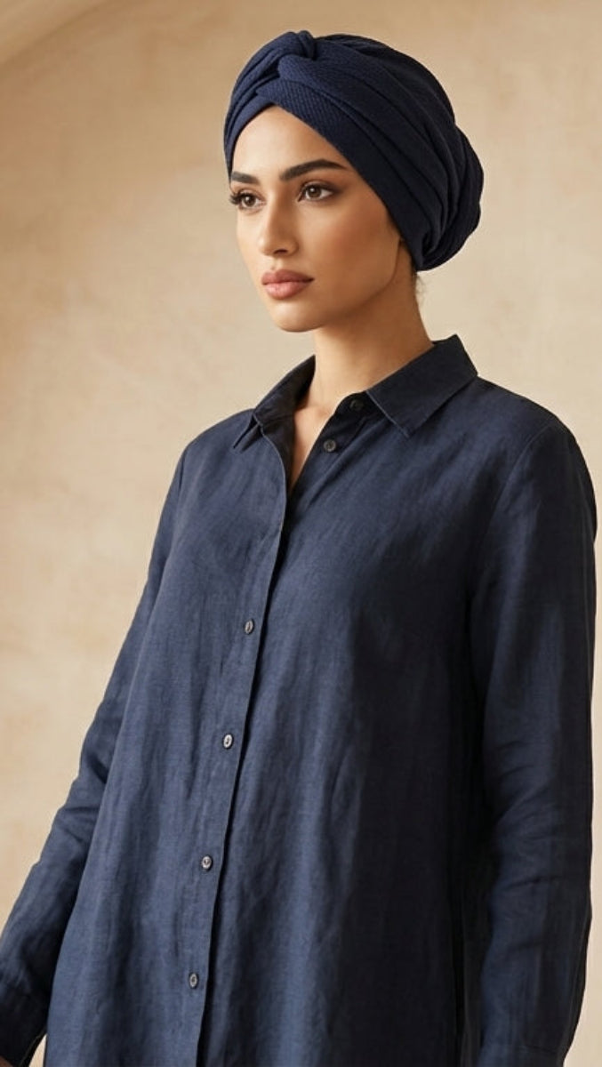 Woman wearing a navy blue shirt and headscarf against a beige wall.