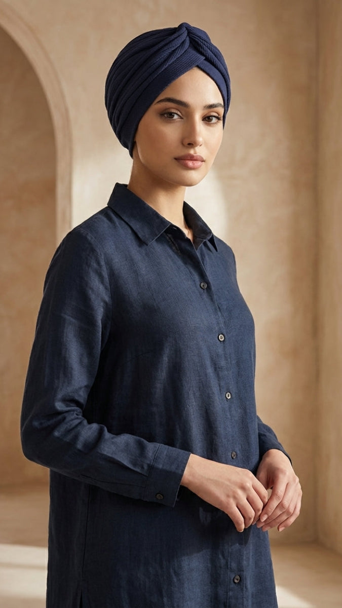 Woman wearing a navy blue shirt and turban in a sunlit room with arched windows.