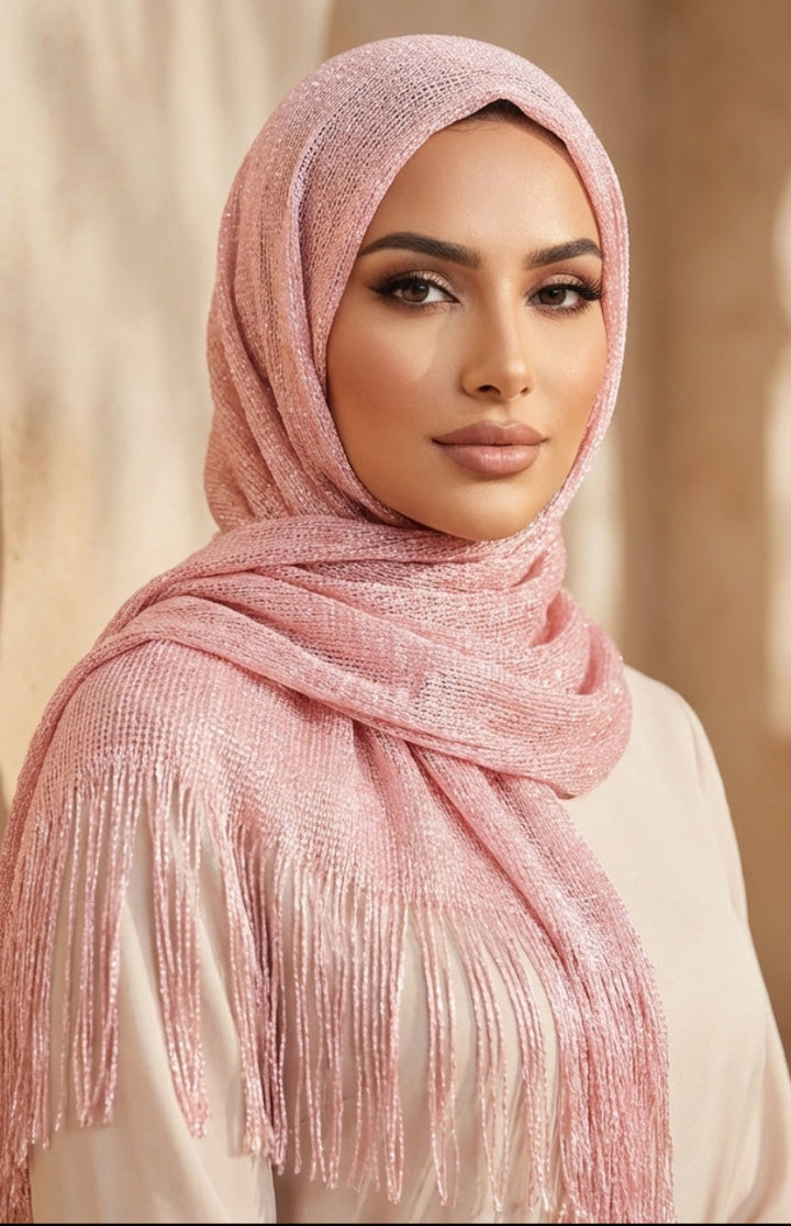 Woman wearing a pink hijab with fringe details against a beige wall.