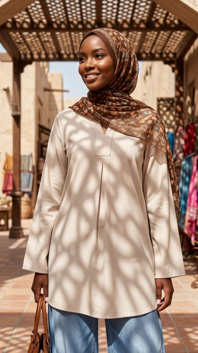 Woman wearing a hijab standing in a sunlit courtyard with architectural elements and plants.