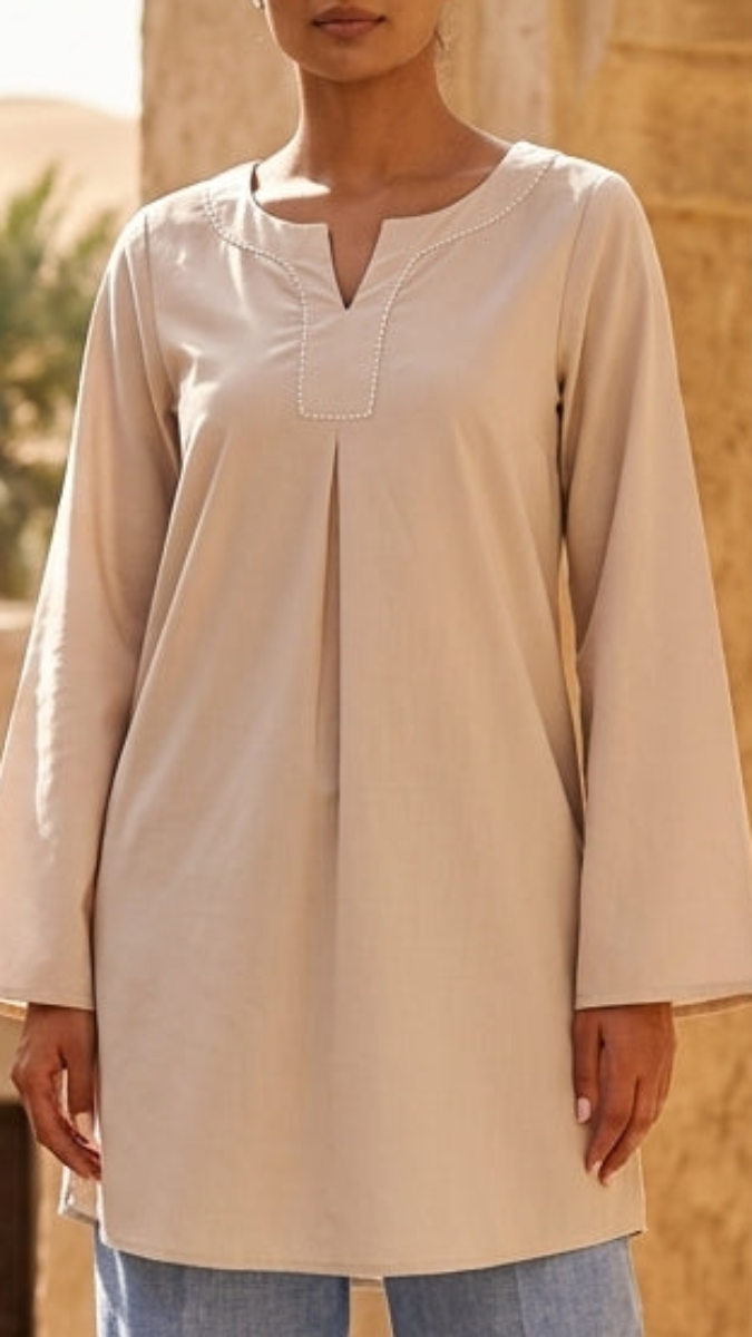 Woman in a beige top and blue pants standing in a desert setting with arched stone buildings.