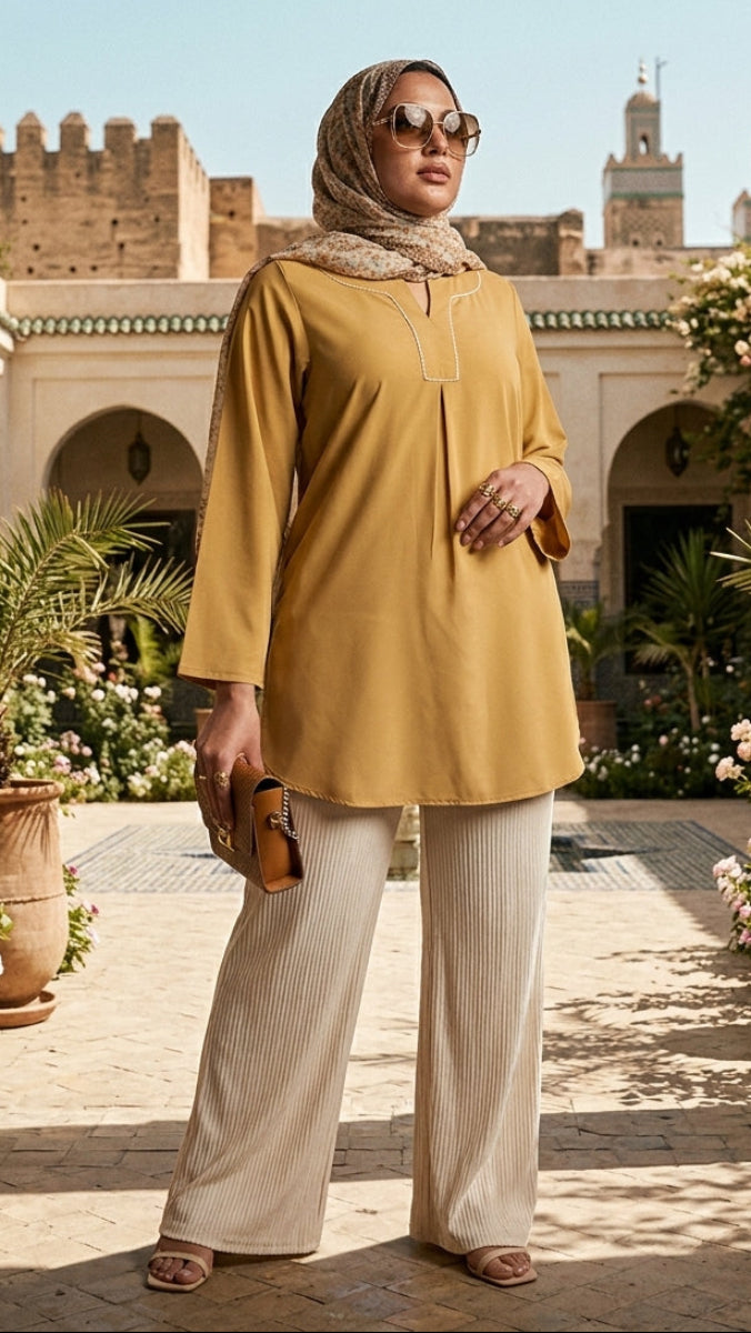 Woman in a yellow top and beige hijab standing in a decorative courtyard with architectural elements and plants.