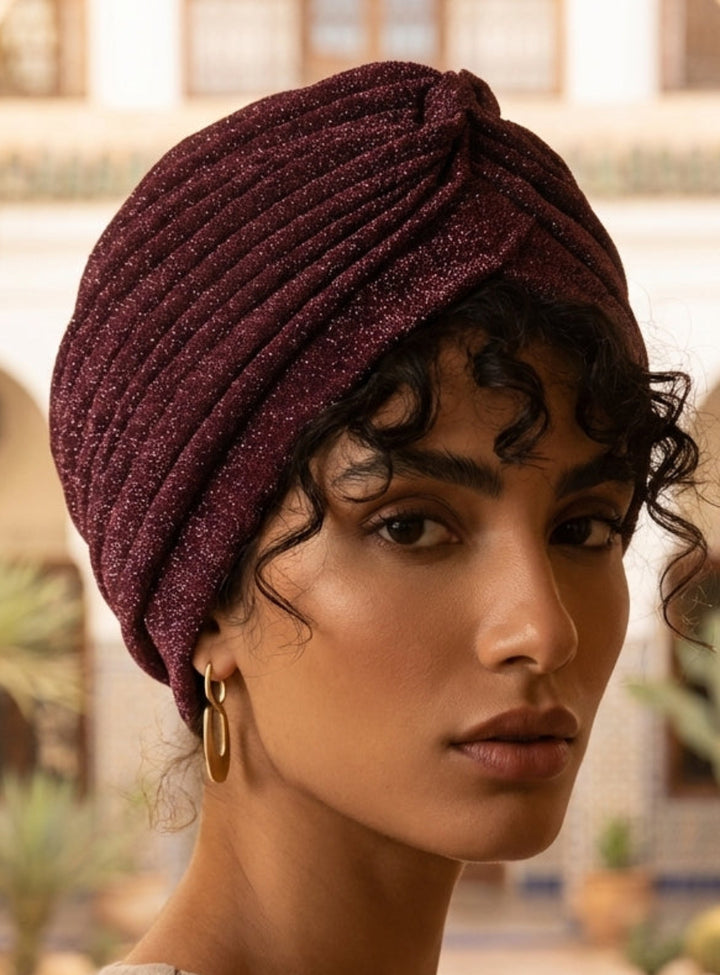 Woman wearing a maroon turban in an outdoor setting with decorative arches and plants.
