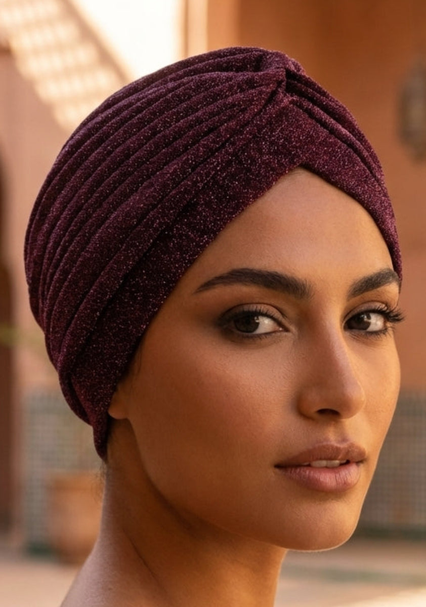 Woman wearing a maroon headscarf in a sunlit outdoor setting with architectural elements.