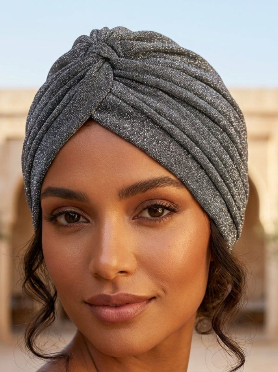 Woman wearing a gray turban in an outdoor setting with arches and plants.