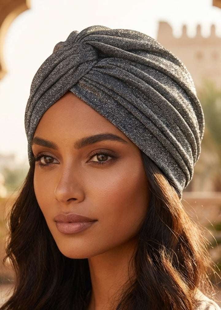 Woman wearing a gray headscarf in an outdoor setting with plants and architectural elements.