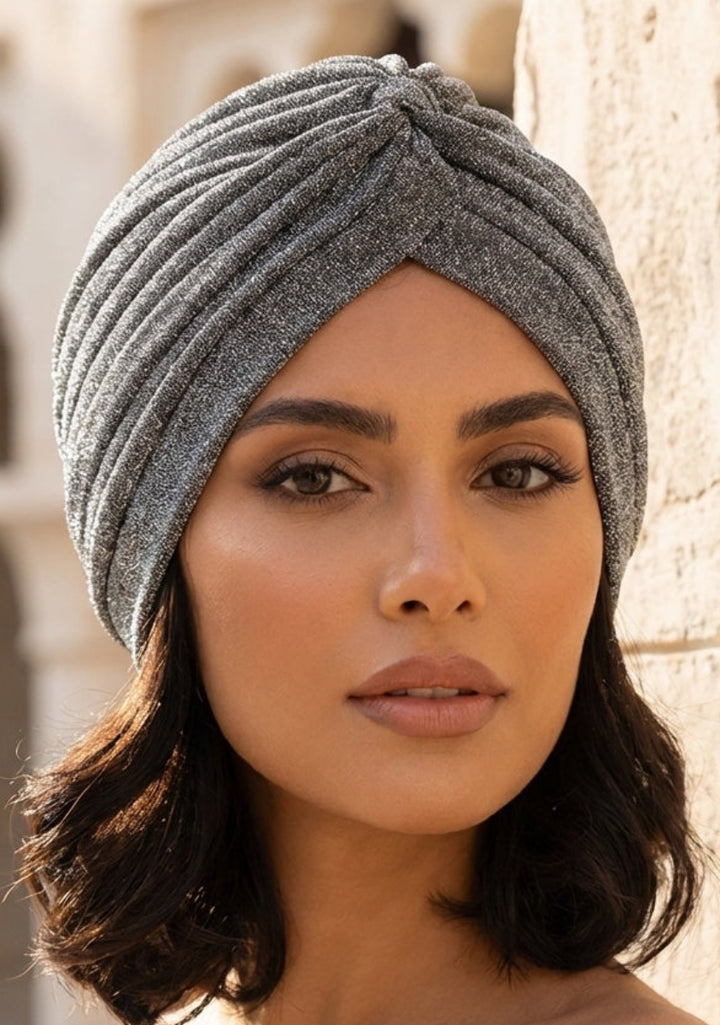 Woman wearing a gray turban against a stone wall background