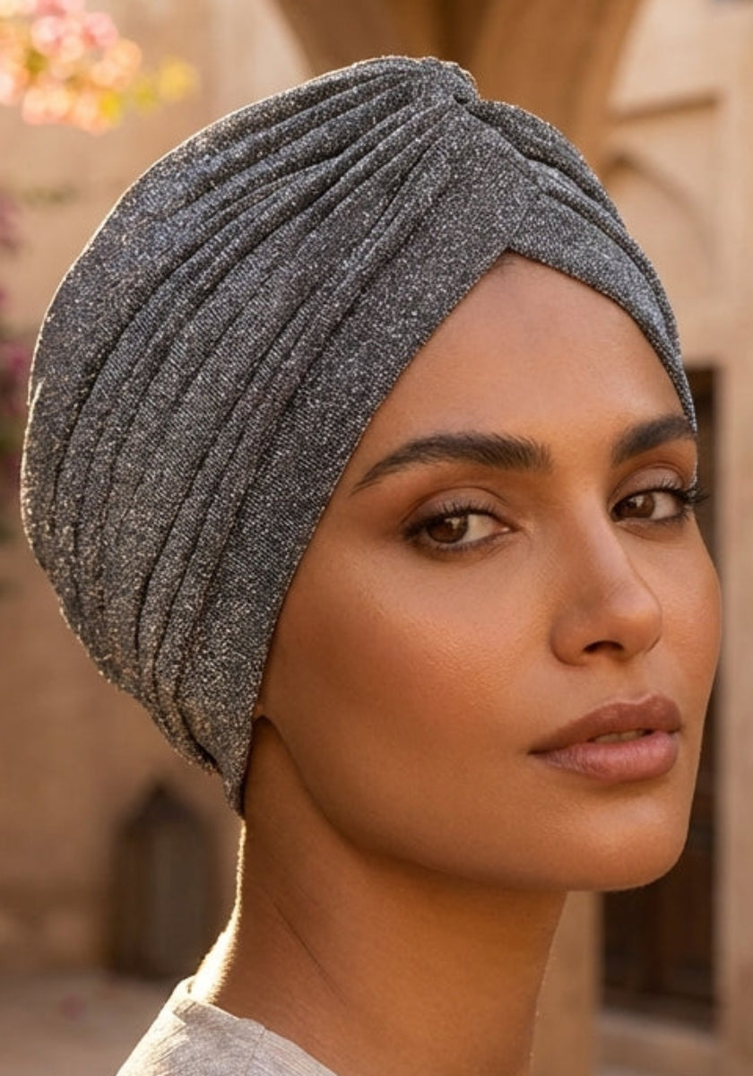 Woman wearing a gray headscarf in an outdoor setting with arches and flowers.