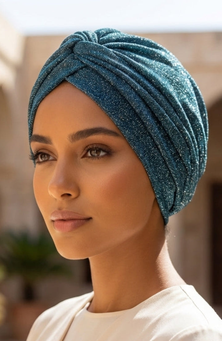 Woman wearing a blue headscarf in an outdoor setting with plants and arches.