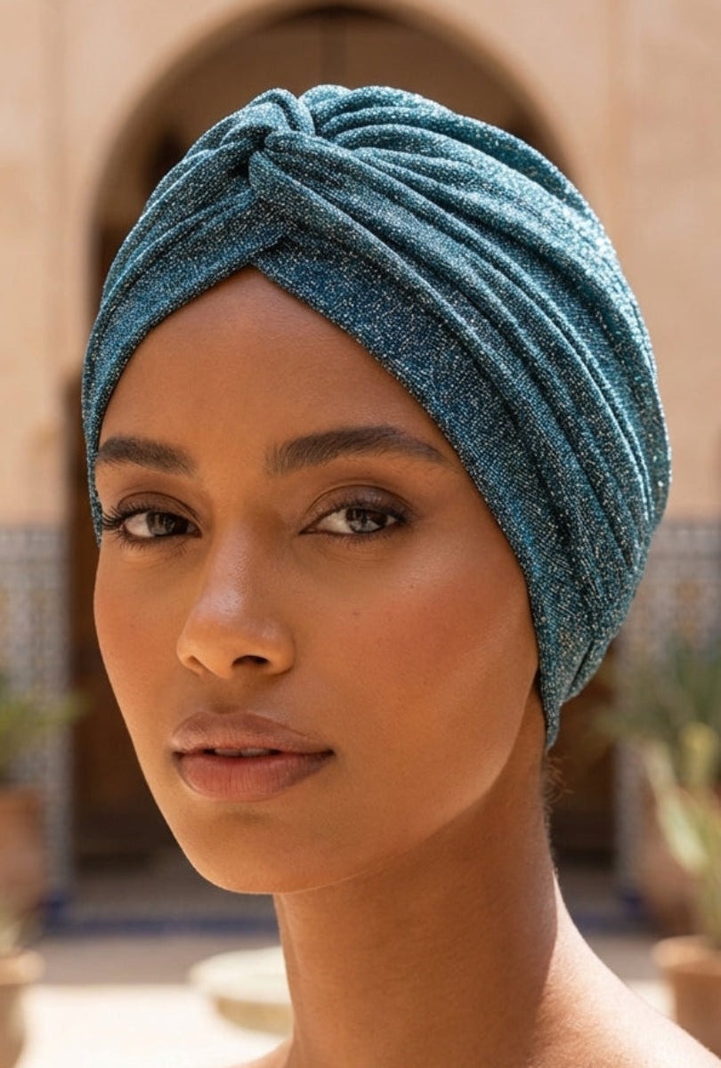 Woman wearing a teal sparkly turban in an outdoor setting with arches and plants.