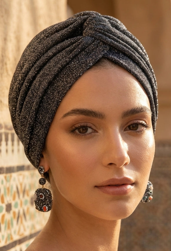Woman wearing a textured silver turban in a sunlit outdoor setting with architectural elements.