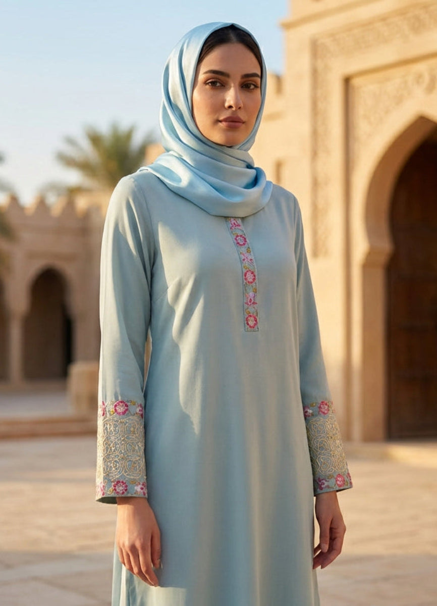 Woman in a light blue dress with floral embroidery standing in front of an architectural structure.