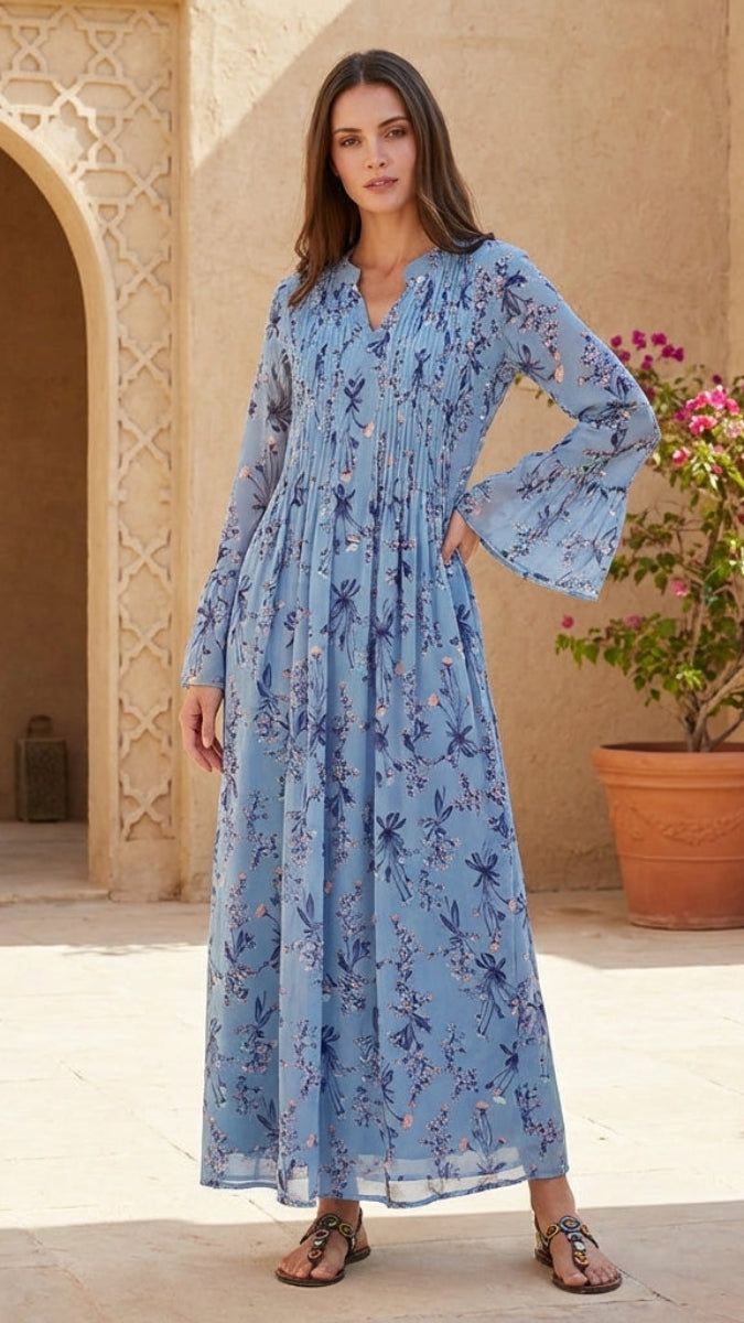 Woman in a blue floral dress standing in a sunlit outdoor setting with arches and plants.