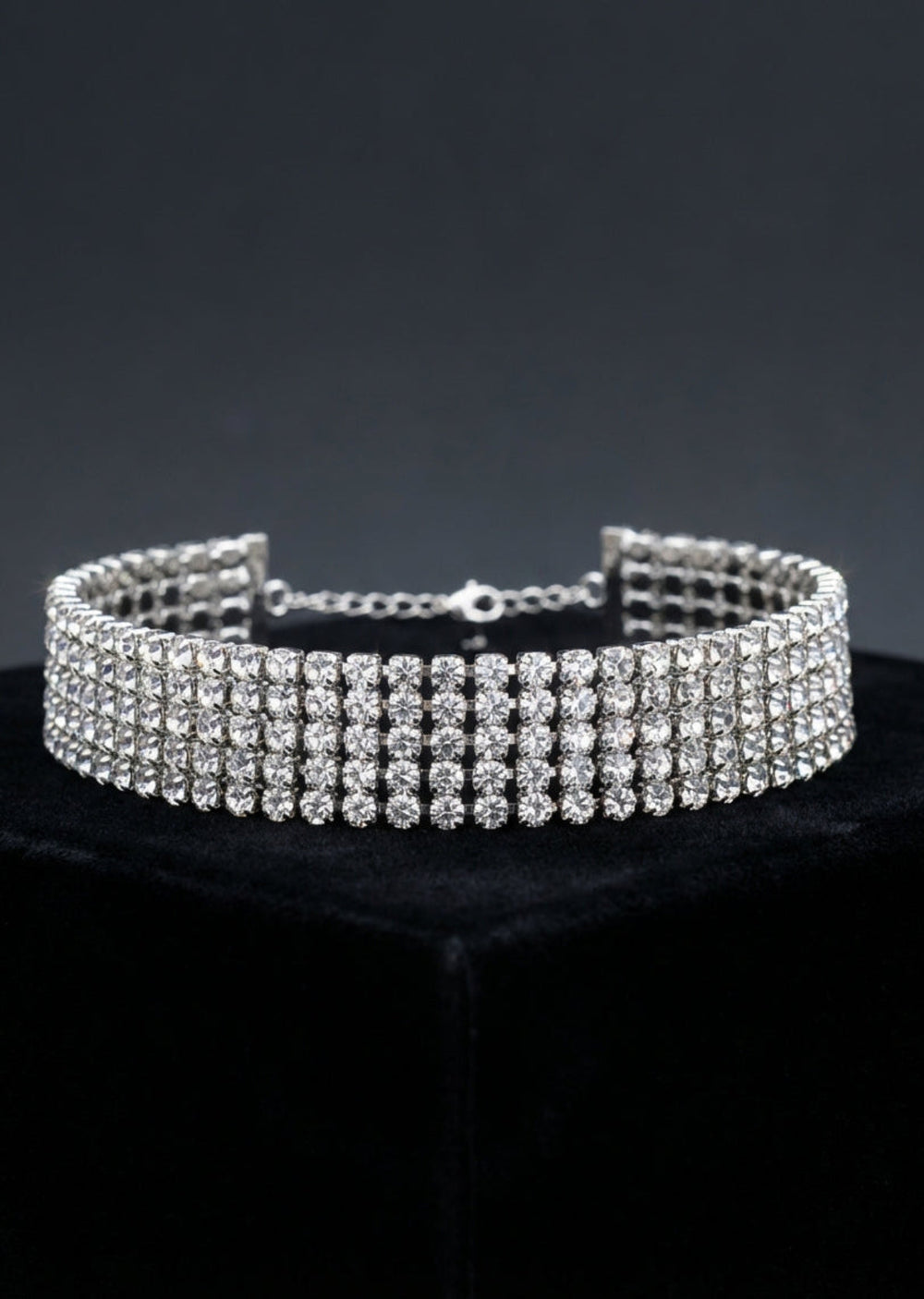Silver choker necklace with clear stones on a black stand against a dark background