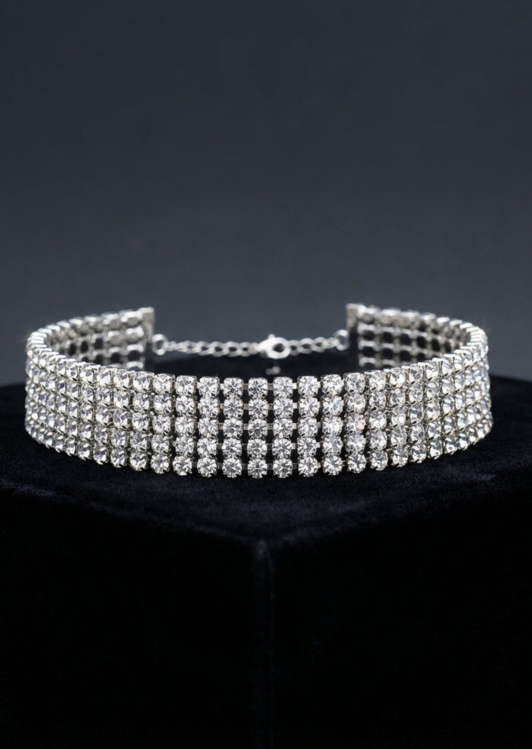 Silver choker necklace with clear stones on a black stand against a dark background