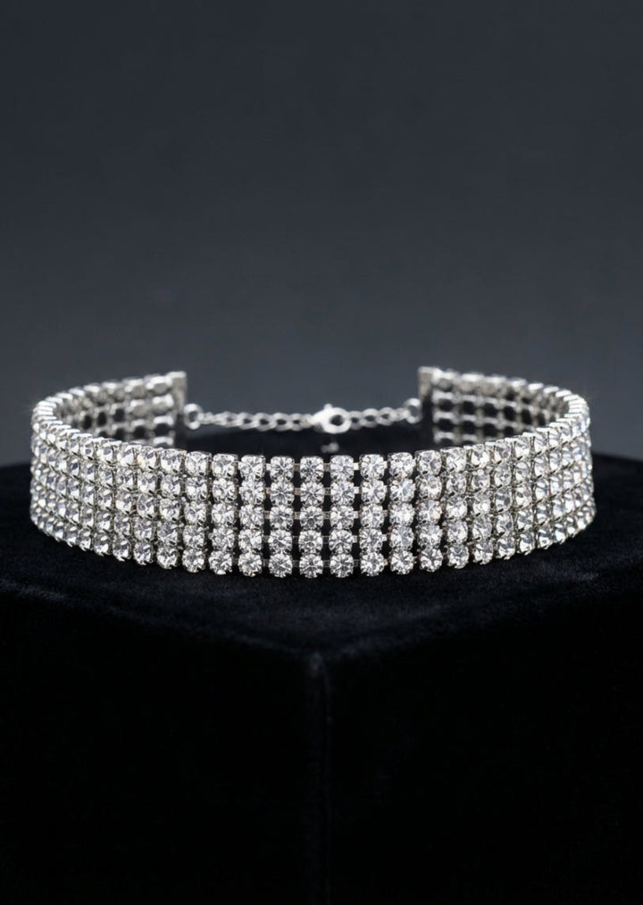 Silver choker necklace with clear stones on a black stand against a dark background