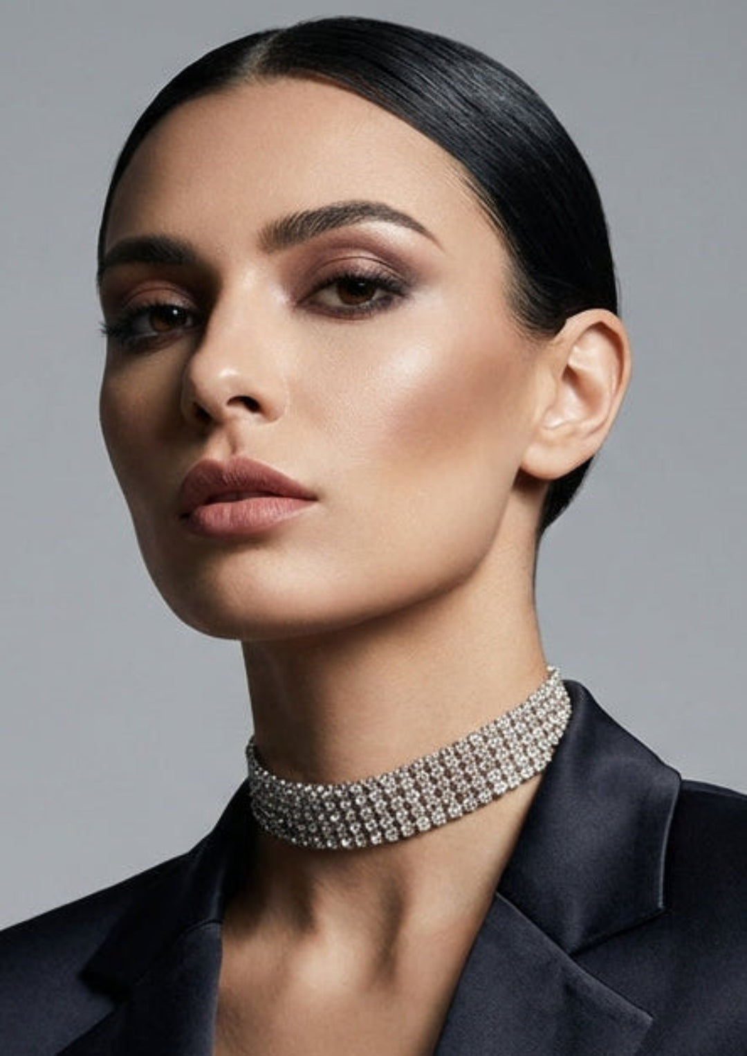 Woman wearing a black blazer and sparkling necklace against a gray background