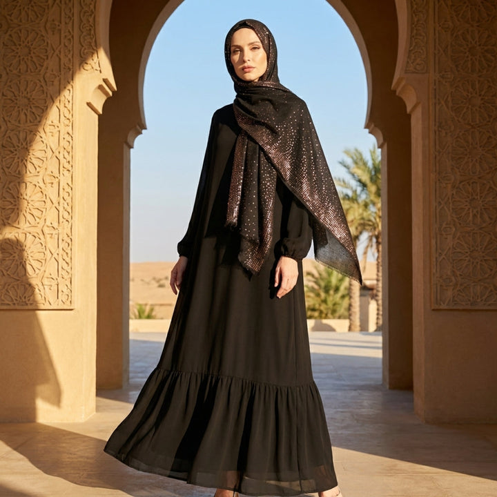 Woman in a black dress and headscarf standing in front of an archway with a desert landscape.