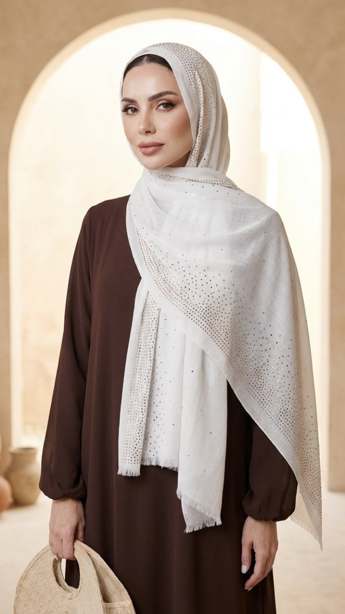 Woman wearing a white hijab with intricate patterns in a warm-toned interior setting