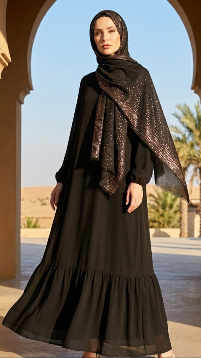 Woman in a black dress and headscarf standing in front of an archway with a desert landscape.
