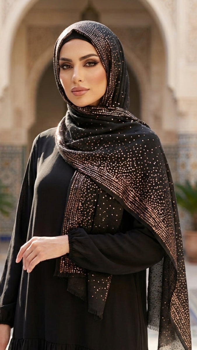 Woman wearing a black abaya with a patterned hijab in an outdoor setting with arches and plants.
